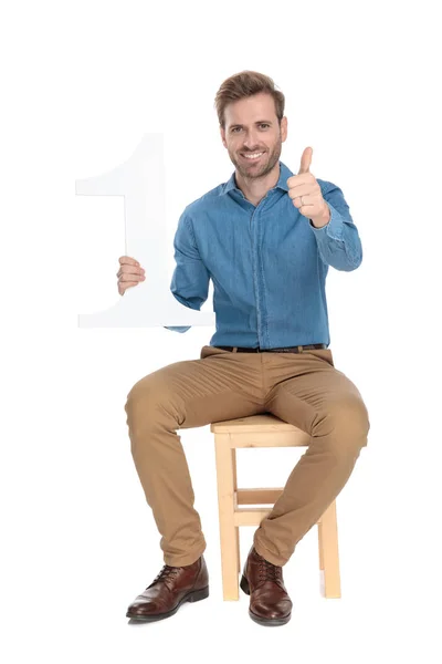 Hombre positivo sosteniendo un número uno, dando un pulgar hacia arriba — Foto de Stock
