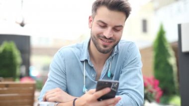 gülümseyen rahat adam restoranda oturur ve cep telefonundan besleme okur