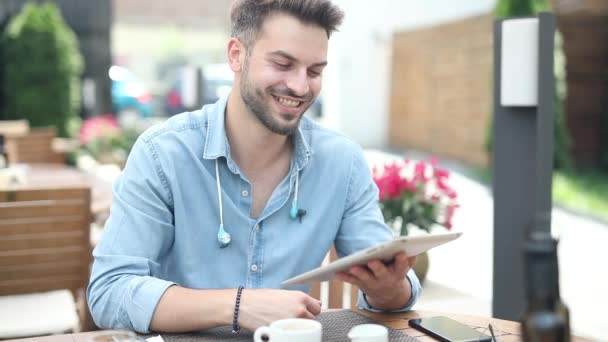 Happy casual man zit in restaurant en leest goed nieuws op zijn Tablet pad computer en maakt OK duim omhoog hand teken — Stockvideo