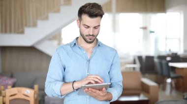 genç rahat adam bir tablet üzerinde çalışmak ve ciddi görünüyor