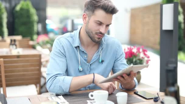 Χαρούμενος casual άνθρωπος κάθεται στο εστιατόριο και διαβάζει καλά νέα στον υπολογιστή του tablet pad και γιορτάζει ήσυχα με χειρονομία χεριού — Αρχείο Βίντεο