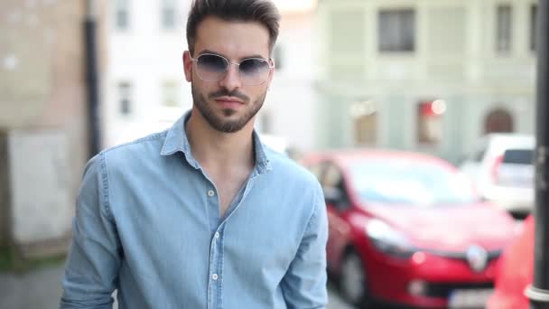 Ung casual man poserar på gatan i en gammal stad, bär solglasögon och blå jeans skjorta — Stockvideo