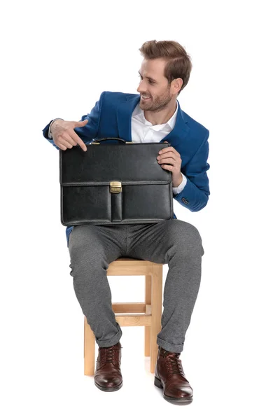 Lustiger Geschäftsmann zeigt auf seine Aktentasche und lächelt — Stockfoto