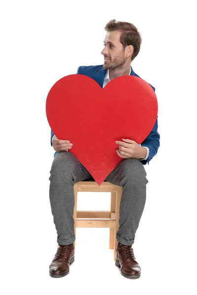 Neşeli rahat adam bir kalp şekli tutan ve yan lara bakıyor — Stok fotoğraf