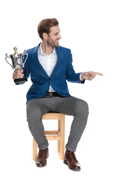 Attractive casual man pointing sideways and holding a trophy — Stock Photo, Image