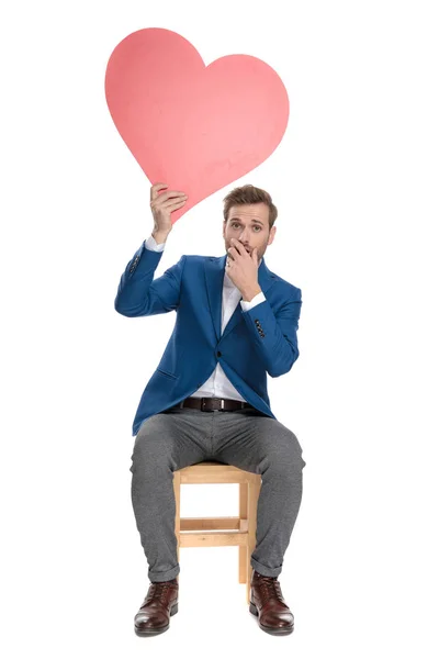 Verraste casual man die een hart vorm boven zijn hoofd vasthoudt — Stockfoto