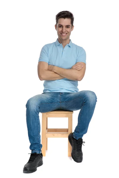 Jeune homme positif assis avec les bras croisés et souriant Image En Vente