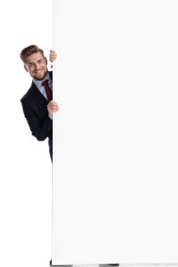 Boş bir reklam panosunun arkasından gülümseyen pozitif işadamı 