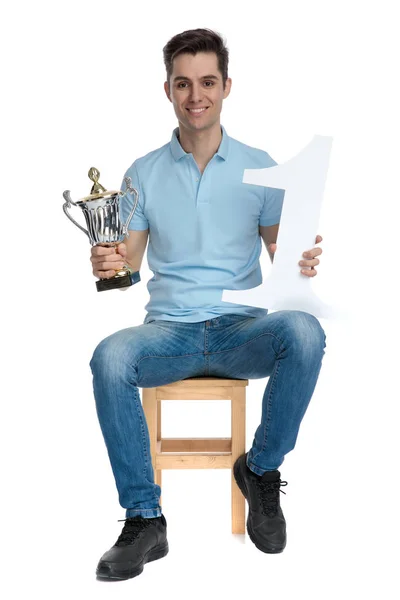 Jovem feliz segurando um troféu e um número um — Fotografia de Stock