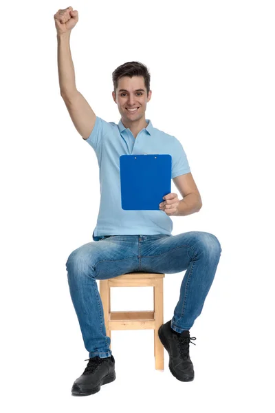 Schöner Student feiert und hält einen blauen Notizblock in der Hand — Stockfoto