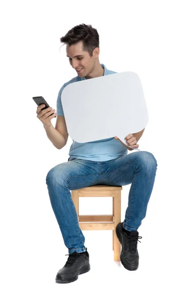 Casual guy texting and holding a blank speech bubble — Stock Photo, Image