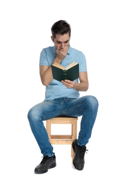 Потрясенный случайный парень, читающий книгу и закрывающий рот — стоковое фото
