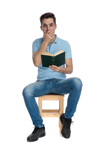 Homem casual espantado cobrindo sua boca e segurando um livro — Fotografia de Stock