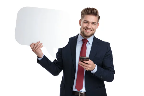 Joven empresario sosteniendo una burbuja de discurso en blanco y su teléfono —  Fotos de Stock