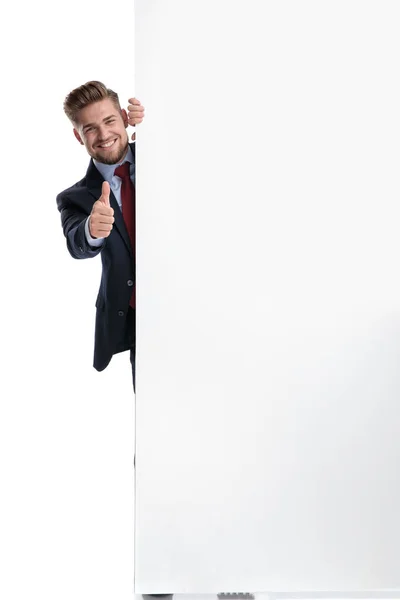 Glücklicher Geschäftsmann gestikuliert hinter einer leeren Plakatwand — Stockfoto