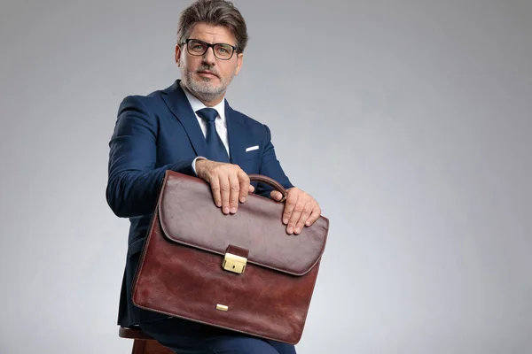Confident businessman holding his briefcase while sitting