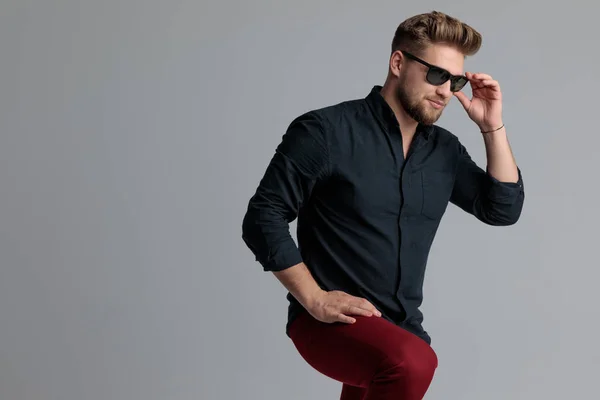 Pensive casual man arrangerar sina solglasögon och tittar bort — Stockfoto
