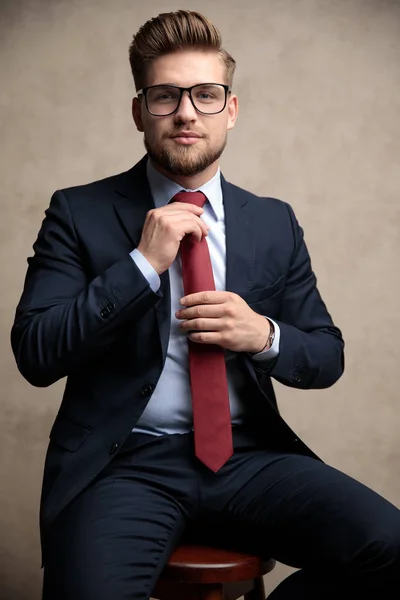 Pewny siebie biznesmen ustalając swój czerwony krawat podczas noszenia okularów — Zdjęcie stockowe