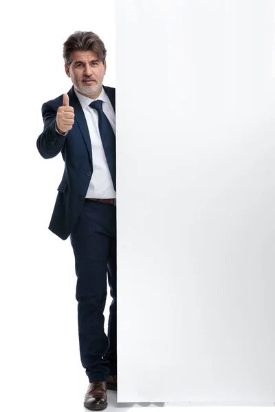 Attraente uomo d'affari gesticolando bene accanto a un cartellone bianco — Foto Stock