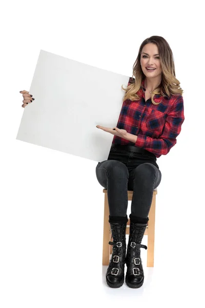 Περιστασιακή γυναίκα κάθεται και παρουσιάζοντας μια κενή αφίσα — Φωτογραφία Αρχείου