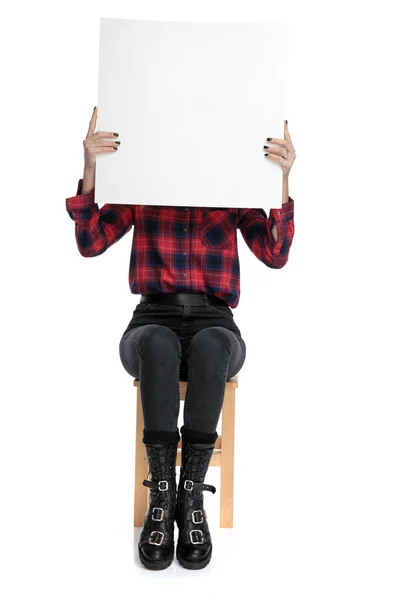 Casual woman sitting with face covered by billboard — Stock Photo, Image