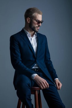 cool young seated man wearing navy suit and sunglasses clipart