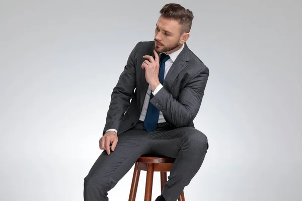 Pensive young businessman sitting on stool and wonders — Stock Photo, Image