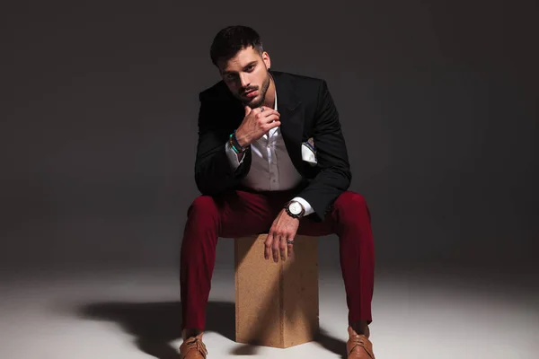 木製の箱の上に座っているペンシブな若い魅力的な男 — ストック写真