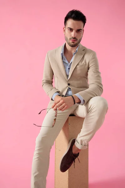 Hombre casual inteligente sentado en una caja de madera con gafas en su han —  Fotos de Stock