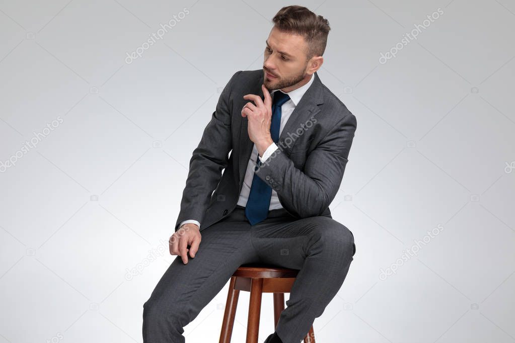 pensive young businessman sitting on stool and wonders 