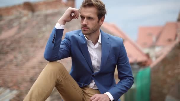 Side view of a pensive seated modern man looking away and at the camera in the city — Stock Video