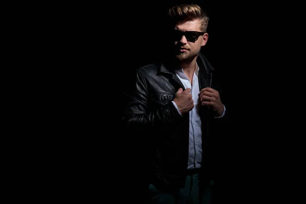Homem sério em jaqueta de couro e óculos de sol olha para o lado — Fotografia de Stock