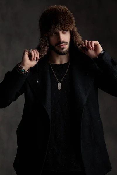 Joven guapo sosteniendo su sombrero de piel sobre fondo gris — Foto de Stock