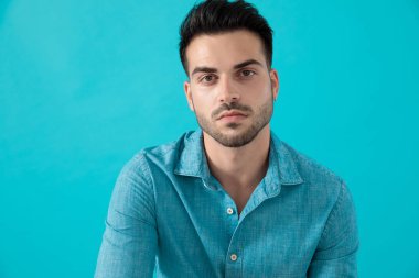 mavi gömlekli adam oturuyor ve ciddi bir şekilde ileriye bakıyor