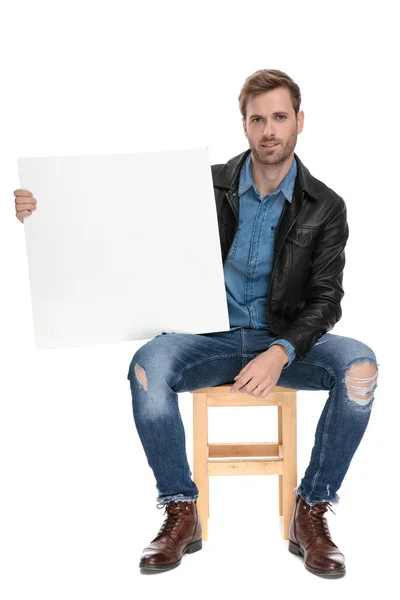 Sitzender Mann mit einer leeren Plakatwand in der einen Hand — Stockfoto