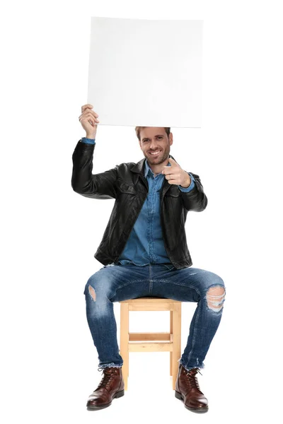 Sitzender Mann, der eine Plakatwand über dem Kopf hält und nach vorne zeigt — Stockfoto