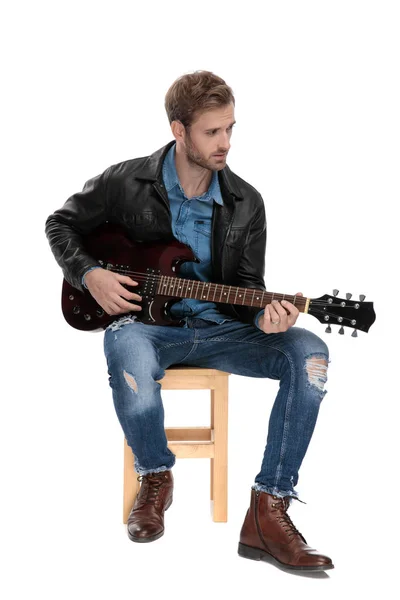 Siedzący człowiek grając na gitarze i patrząc od — Zdjęcie stockowe