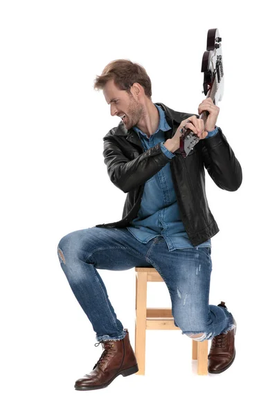 Sittande man kastar sin gitarr arg — Stockfoto
