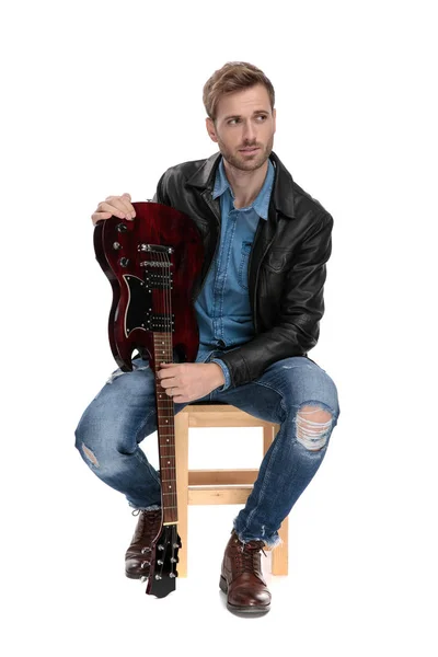 Siedzący mężczyzna trzyma gitarę do góry nogami — Zdjęcie stockowe