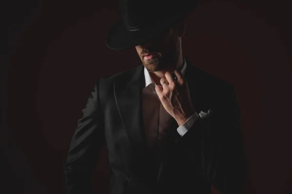 Mysterious young man fixing collar on black background — Stock Photo, Image