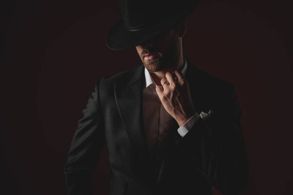 mysterious young man fixing collar on black background