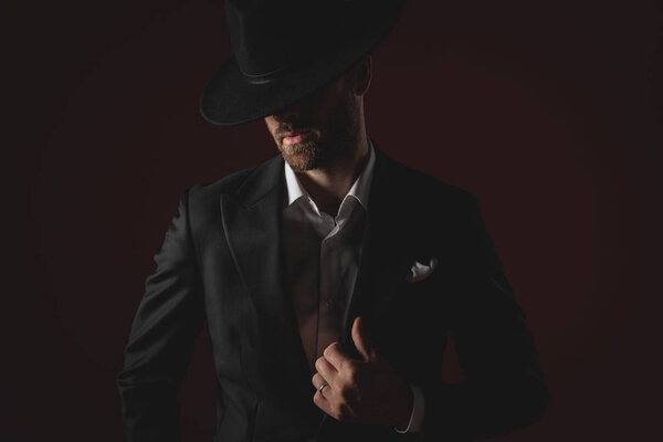 attractive man wearing tuxedo and hat fixing collar