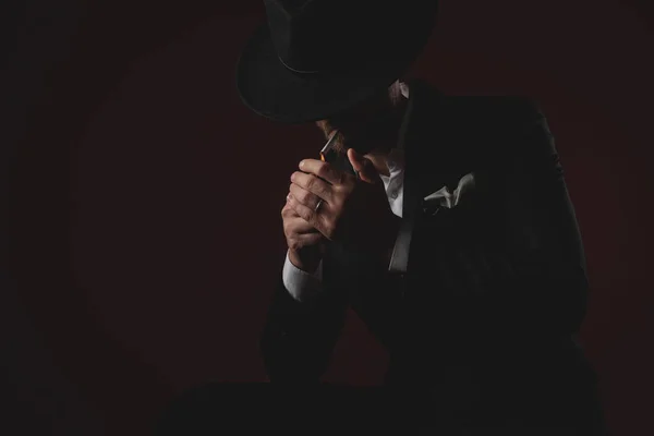 Tajemný mladý muž osvětlovací cigaretu na černém pozadí — Stock fotografie