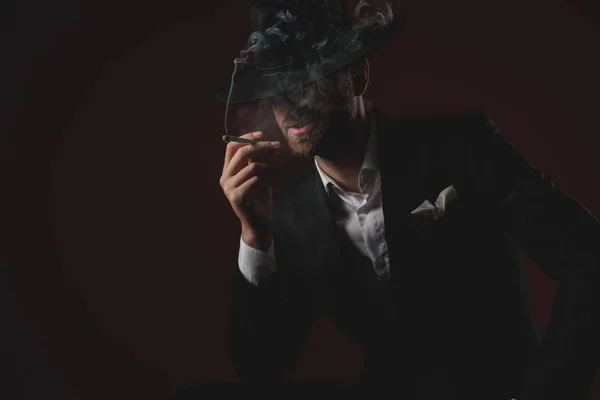 Uomo misterioso in smoking fumo su sfondo nero — Foto Stock