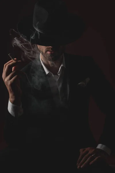 Привабливий молодий чоловік курить і сидить на чорному тлі — стокове фото