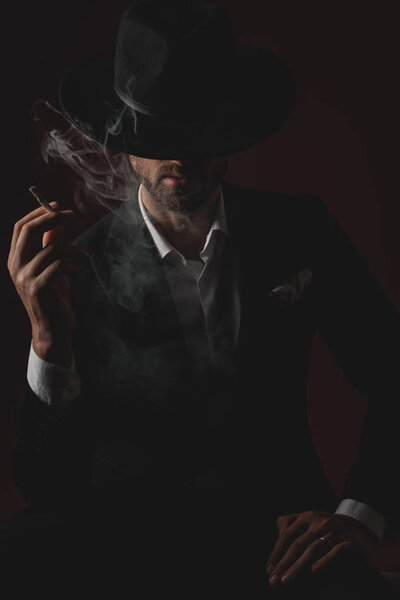 attractive young man smoking and sitting on black background
