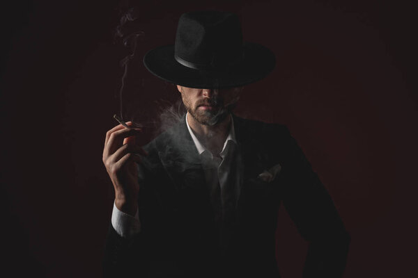 enigmatic young man smoking on black background