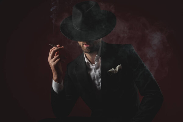 attractive young man in tuxedo smoking on black background