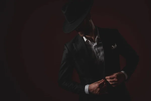Mysterious young man arranging his coat on black background — Stock Photo, Image