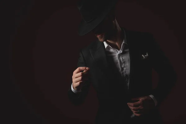 Mysterious young man fixing coat on black background — Stock Photo, Image